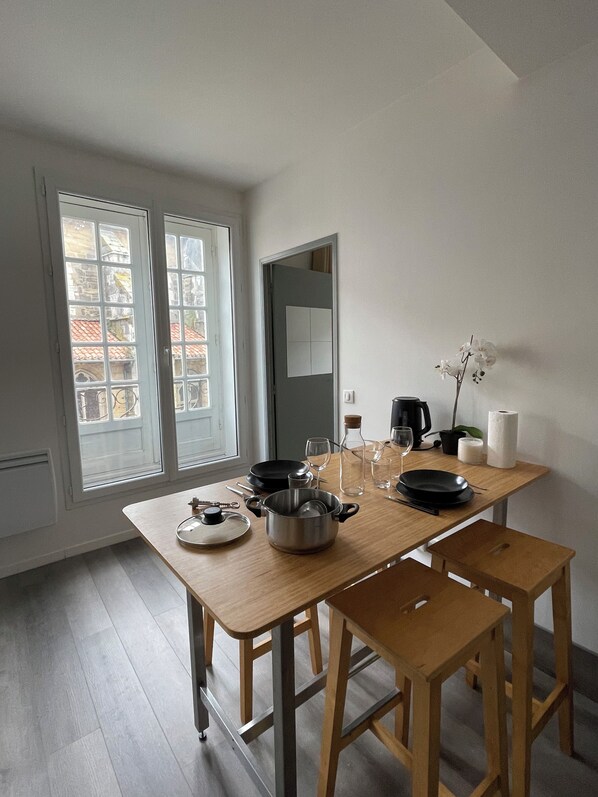 A dining area with a wooden table, two chairs, a coffee maker, and a window with a view of buildings. - Apartment on Hugues Street (Bayonne)