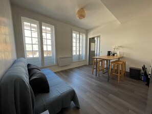 A modern living space with a sofa, a dining table with stools, and large windows. - Apartment on Hugues Street (Bayonne)