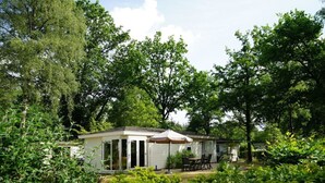 A single-story mobile home with a patio area, surrounded by dense greenery and trees. - Holiday Home in Arnhem With Terrace (Arnhem)