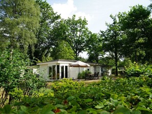 A single-story mobile home with a patio area, surrounded by dense greenery and trees. - Holiday Home in Arnhem With Terrace (Arnhem)