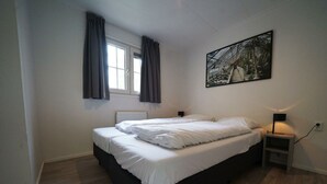 A bedroom with a bed, a window with curtains, a nightstand with a lamp, and a painting on the wall. - Holiday Home in Arnhem With Terrace (Arnhem)