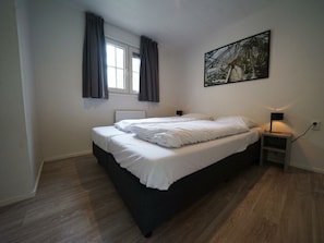 A bedroom with a bed, a window with curtains, a nightstand with a lamp, and a painting on the wall. - Holiday Home in Arnhem With Terrace (Arnhem)