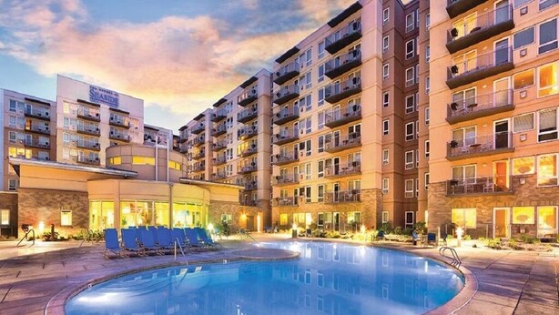 Ein Hotel mit Schwimmbad, mehreren Balkonen und einer gut beleuchteten Fassade.