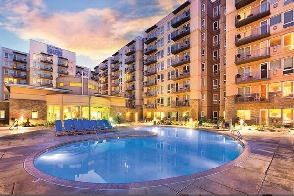 A hotel with a swimming pool, multiple balconies, and a well-lit exterior.