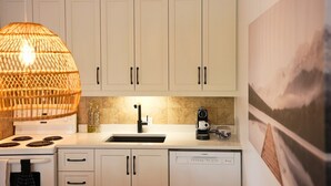 A kitchen with white cabinets, a stove, a sink, a coffee maker, and a hanging light fixture. - O` Bord du Lac Memphrémagog (Magog)