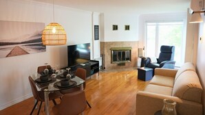 A modern living room with a TV, fireplace, dining area, and seating. - O` Bord du Lac Memphrémagog (Magog)