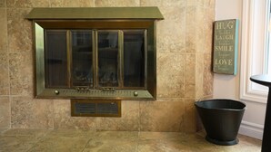 A fireplace with a metal frame and glass doors, a small vent below it, and a decorative sign on the wall. - O` Bord du Lac Memphrémagog (Magog)