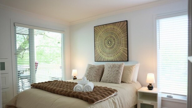A bedroom with a bed, two bedside tables, a wall-mounted artwork, and a view through the window. - O` Bord du Lac Memphrémagog (Magog)