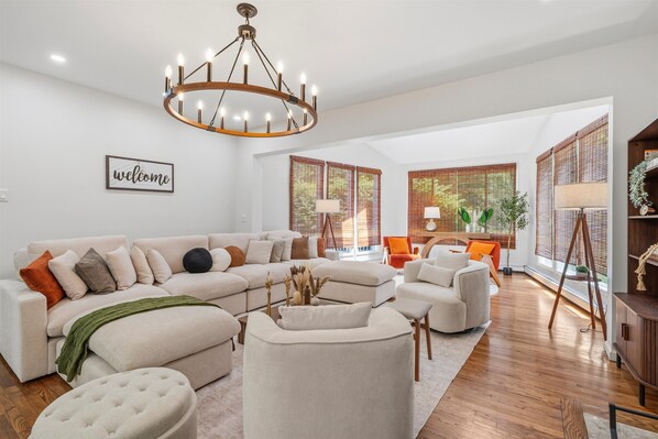 A spacious living room with a sectional sofa, a round coffee table, and a chandelier.