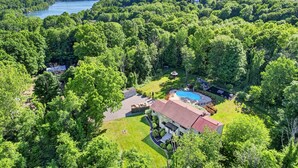 En stor bolig med swimmingpool, omgivet af tæt skov og en sø.