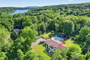 A large house with a swimming pool, surrounded by dense forest and a lake.