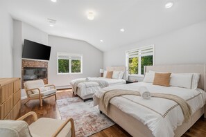 A bedroom with two beds, a TV, a wooden cabinet, and a chair.