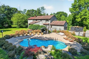 A large house with a swimming pool, surrounded by a well-maintained lawn and trees.