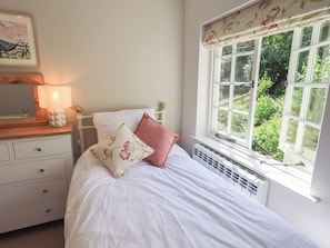 Quarto com cama, mesa de cabeceira com abajur, radiador e janela com vista para áreas verdes.
