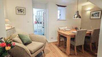 Una sala de estar acogedora con sofá, una mesa de comedor con sillas, una cocina al fondo y una escalera.