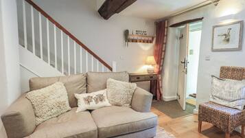 A living room with a beige sofa, a wooden coffee table, a wicker chair, a staircase, and a door leading to another room.