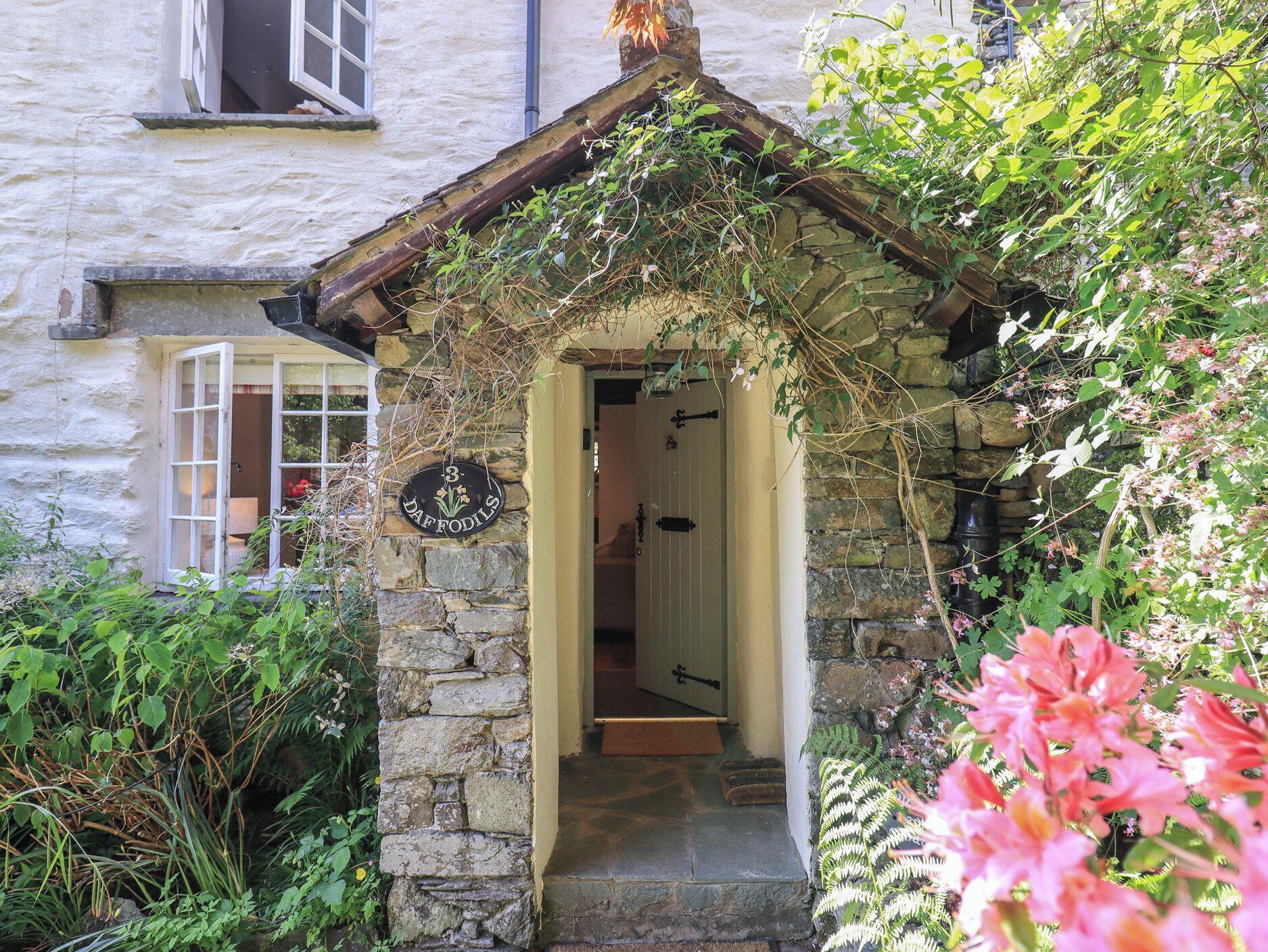 Ein Steinhaus mit einer Tür, auf der 'DAFFODILS' steht, und einem kleinen Veranda-Bereich.