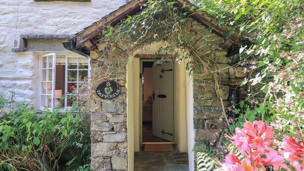 Une maison en pierre avec une porte sur laquelle on peut lire le mot «DAFFODILS» et un petit porche.