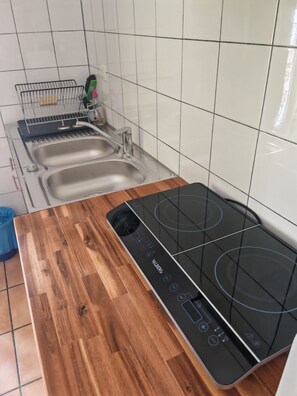 Eine Küche mit einer Holzarbeitsplatte, einer schwarzen Induktionskochstelle und zwei Edelstahlspülen.