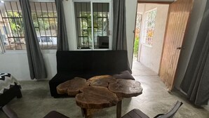 A room with a round wooden table, two chairs, a sofa, and a sliding door leading to an outdoor area. - Located in the heart of Zicatela (Brisas de Zicatela)