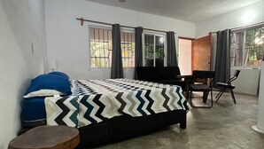 A bedroom with a bed, a desk, and a chair. There is a ceiling fan, windows with curtains, and a view of the outdoors. - Located in the heart of Zicatela (Brisas de Zicatela)