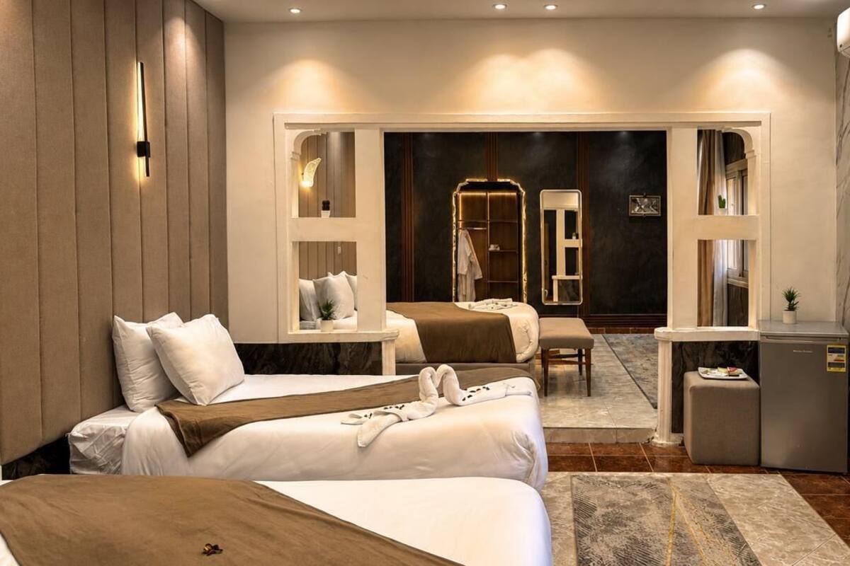 A hotel room with two beds, a desk, a chair, a small table, a mirror, and a refrigerator.