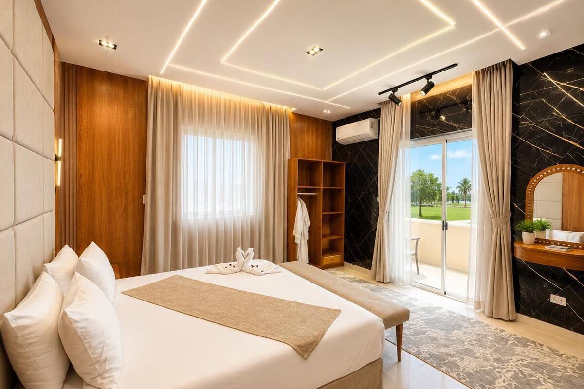 A modern hotel room with a large bed, a wooden wardrobe, a vanity with a mirror, and a view of the outdoors.