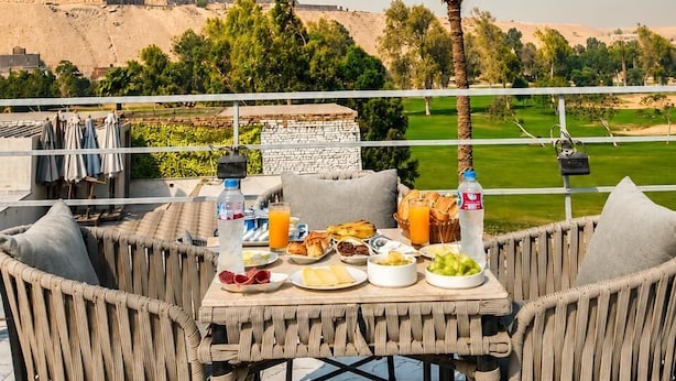 A dining table with food and drinks, a view of a pyramid, and a palm tree. - glow pyramid view (Giza)