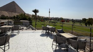 A terrace with outdoor seating, a view of a pyramid, and a clear sky. - glow pyramid view (Giza)