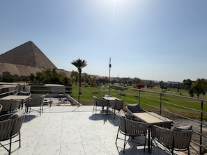 A terrace with outdoor seating, a view of a pyramid, and a clear sky. - glow pyramid view (Giza)