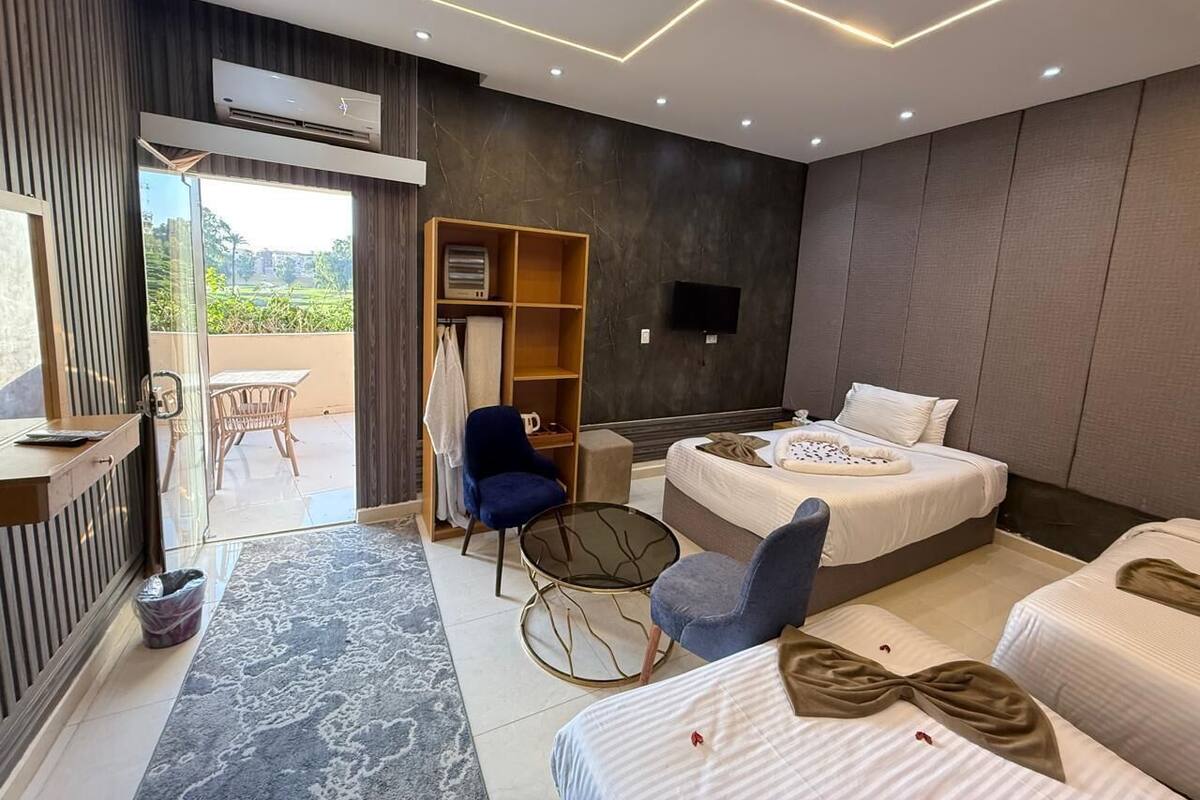 A modern hotel room with a bed, two chairs, a small table, a TV, and a balcony with a table and chairs.