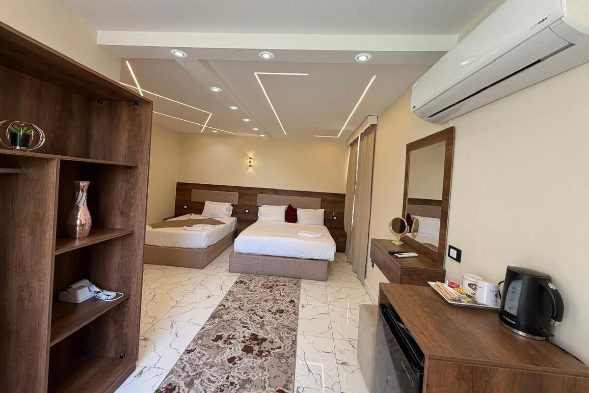 A hotel room with two beds, a wooden wardrobe, a desk with a coffee maker, and an air conditioning unit.