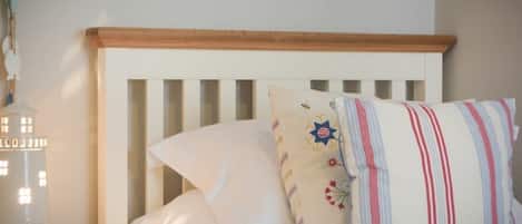 A bed with white bedding and striped pillows, a wooden headboard, and a bedside table with a lamp.