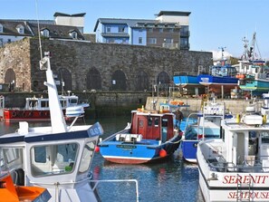 A marina with various boats docked, a stone wall, and a building with arched windows in the background. - Juniper Cottage (Seahouses)
