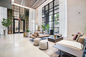 A spacious lobby with a modern design, featuring a large seating area with sofas and ottomans, a coffee table, and potted plants. - Sleek Urban Apartment - Walk to Kaseya Center (Miami)