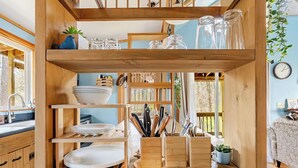 Une étagère de cuisine en bois, sur laquelle sont posées des assiettes, des bols et des ustensiles.