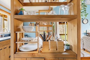 Una estantería de madera con platos, tazones y utensilios de cocina.