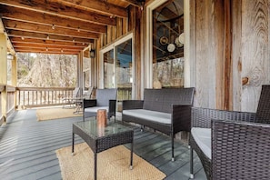 Un espacio exterior techado con mobiliario de mimbre, una mesa de vidrio y vistas al exterior.
