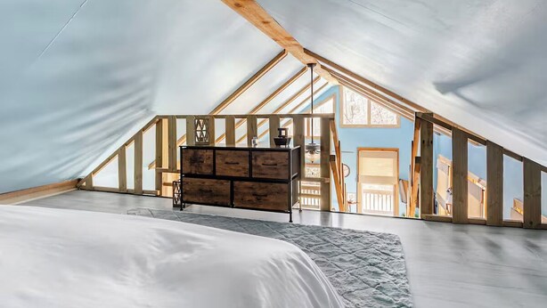 Une chambre avec un plafond en pente, des poutres en bois, un lit et une commode.