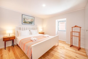 A bedroom with a bed, bedside tables, a wooden floor, a painting on the wall, and a window. - GuestReady - The George (Lisbon)