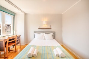 Un dormitorio con cama, escritorio y silla. Hay toallas sobre la cama.