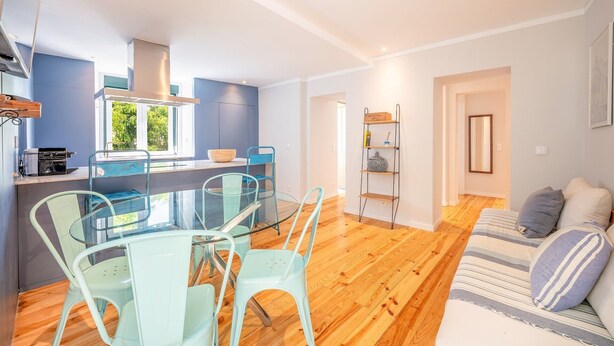 A modern kitchen with a dining area, a sofa, and a bookshelf.