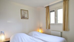 A hotel room with two beds, a window with curtains, a radiator, and a wall-mounted picture. - Unique Nouveau 4 (Otterlo)