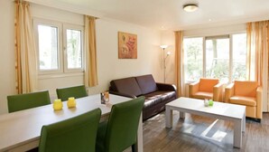 A living room with a brown leather sofa, green chairs, a white coffee table, and a dining table with yellow vases. - Unique Nouveau 4 (Otterlo)
