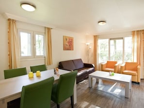 A living room with a brown leather sofa, green chairs, a white coffee table, and a dining table with yellow vases. - Unique Nouveau 4 (Otterlo)