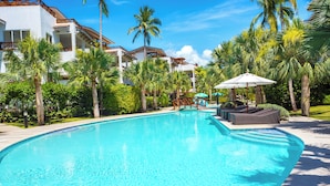 A swimming pool with lounge chairs and umbrellas, surrounded by palm trees and modern buildings. - Unique Penthouse with Huge Private Rooftop & Jacuzzi - Beach & Restaurant Nearby (El Limón)