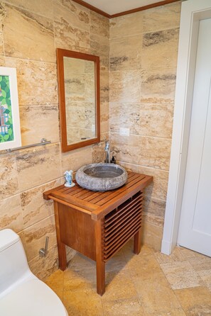 Ein Badezimmer mit einer Steinwand, einem Holzwaschtisch, einem Becken aus Stein und einem Spiegel über dem Waschtisch.