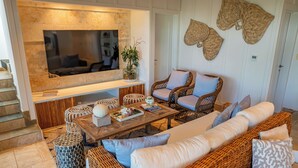 Un salon avec un téléviseur, des meubles en osier, une table basse et un escalier.