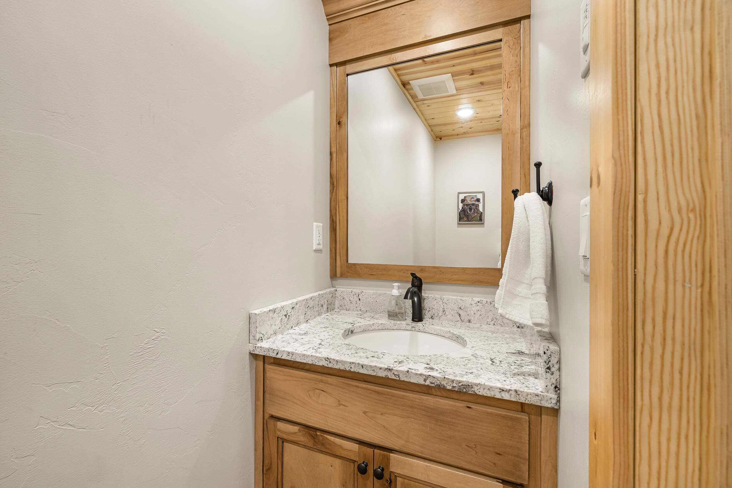 A bathroom with a wooden vanity, a sink, a mirror, and a towel hanging on the wall.
