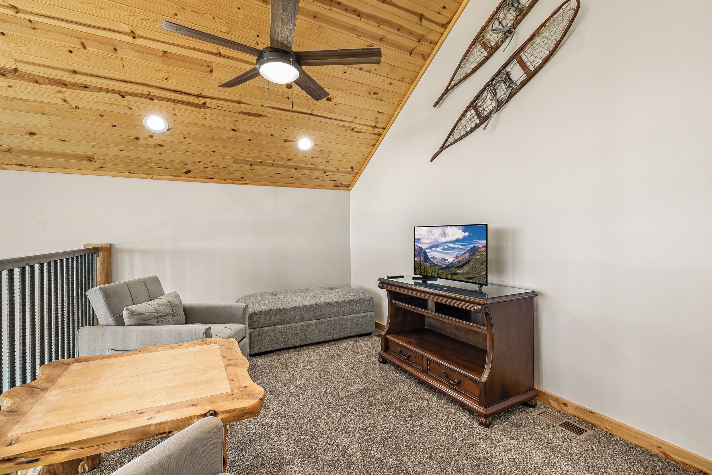 Ein Zimmer mit Deckenventilator, Fernseher auf einem Holzbodenständer, einem grauen Sofa und einem Holztisch.